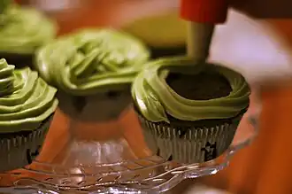 A pastry bag fitted with a star tip being used to frost cupcakes