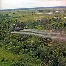 A UH-1D helicopter from the 336th Aviation Company sprays a defoliation agent over farmland in the Mekong Delta.