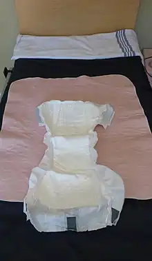 An adult diaper and a pink incontinence pad laid out on top of a single bed