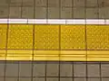 Tactile pavings installed on a platform at a Japanese train station. Horizontal tactile paving at the bottom indicates the 'inner' side, away from the rail tracks.
