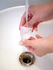 Rinsing a cup under cool, clean running water in a sink. Hot water speeds coagulation and can set bloodstains.