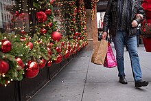 A man carries shopping bags past red and green Christmas decorations